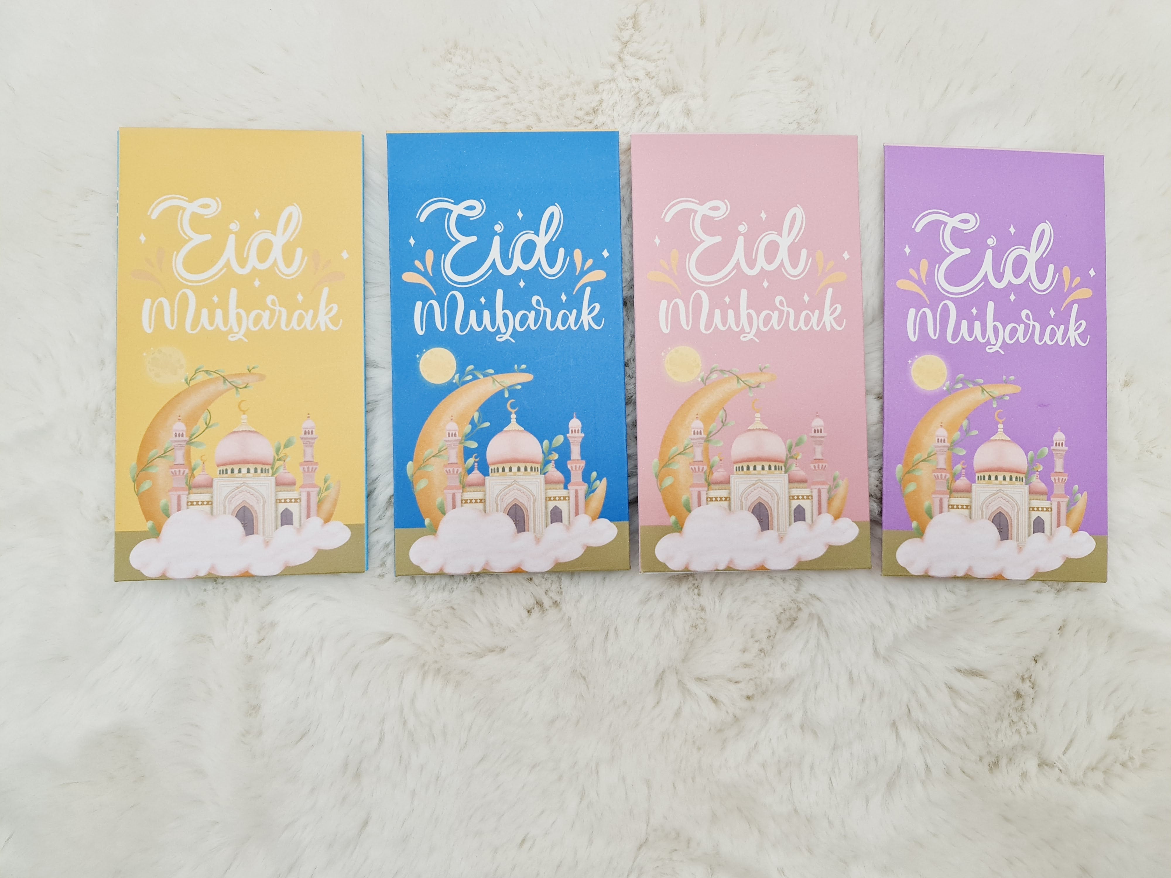 Four colorful greeting cards with 'Eid' wishes on a white fluffy surface